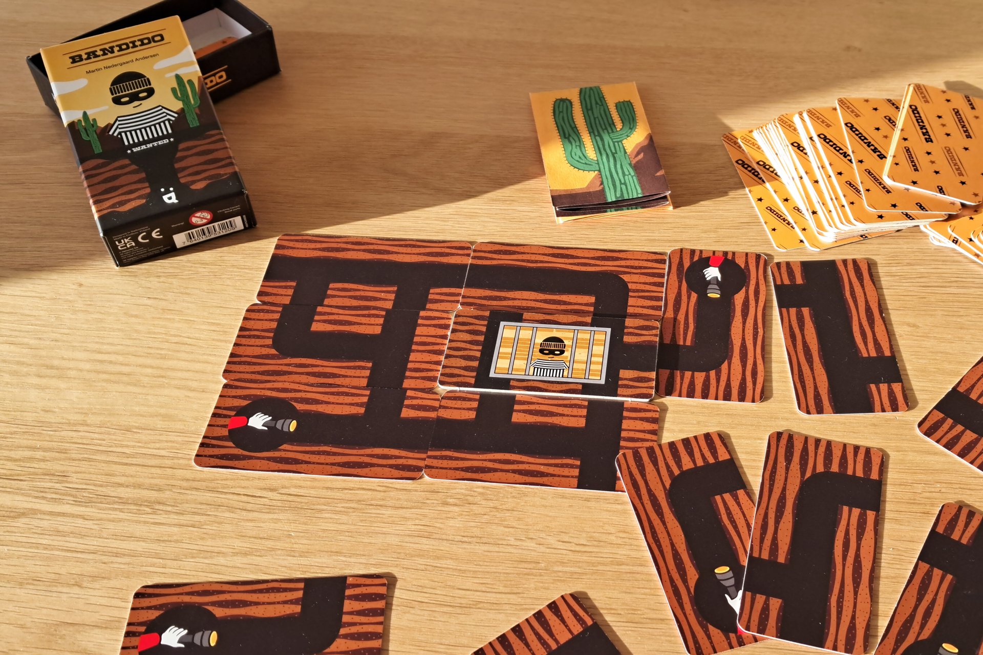 Bandido card game box, mega card with five exits and a quick game played, cards laid around the table