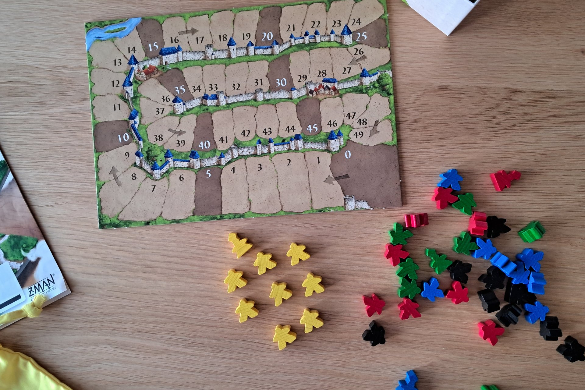 Five sets of wooden Carcassonne meeples in yellow, red, green, blue, and black and the scoring board