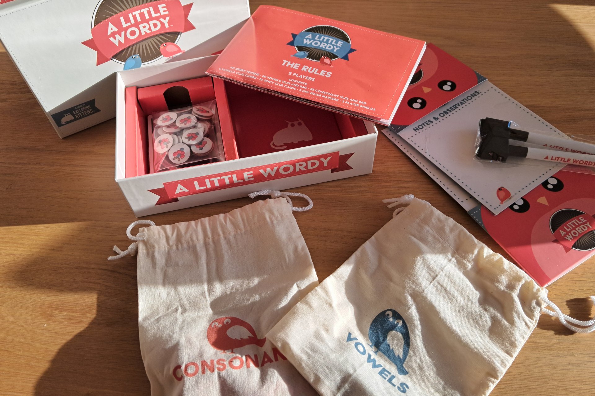 The A Little Wordy game box opened to show all the components inside, including tiles, clue cards, tokens, and boards.